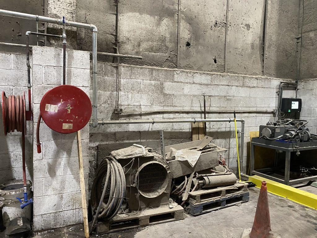 Photo shows a 2" water main installed along a wall. Also shows some fire hose reels wound up on a wall.